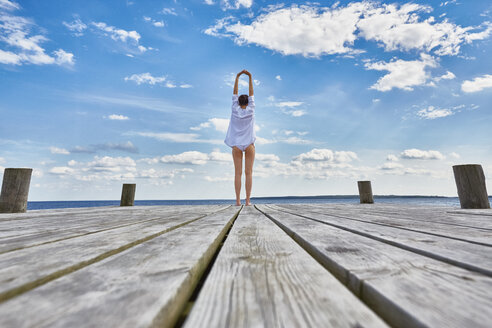 Young woman standing on wooden pier, stretching, rear view - CUF18710