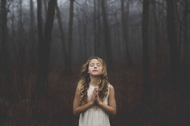 Porträt eines langhaarigen blonden Mädchens mit geschlossenen Augen und zusammengelegten Händen im nebligen Wald - ISF07098