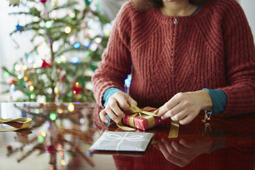 Abgeschnittene Aufnahme einer Frau, die ein Weihnachtsgeschenk am Tisch einpackt - ISF07120