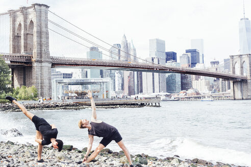 Zwei Männer machen Yoga am Flussufer vor der Brooklyn Bridge, New York, USA - ISF07167