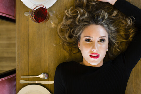 Draufsicht auf eine junge Frau, die auf einem Esstisch liegt, lizenzfreies Stockfoto