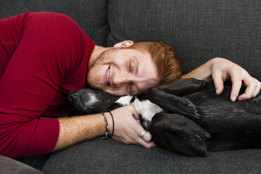 Junger Mann auf dem Sofa liegend, der seinen Hund umarmt, Augen geschlossen und lächelnd - ISF07211