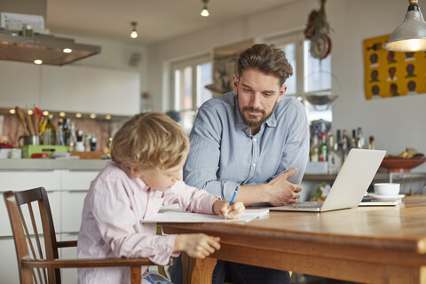 Vater hilft seinem Sohn bei den Hausaufgaben im Home Office, lizenzfreies Stockfoto