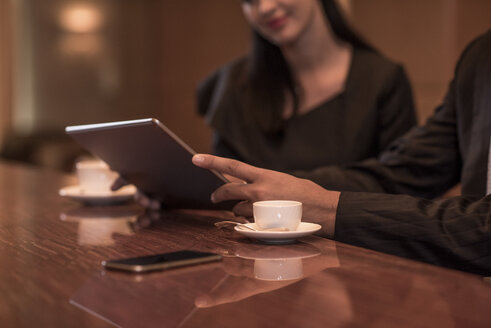 Ausgeschnittene Aufnahme eines Geschäftsmannes und einer Frau, die an der Hotelbar sitzen und ein digitales Tablet benutzen - CUF18947