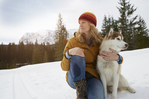 Frau sitzt mit Husky in verschneiter Landschaft, Elmau, Bayern, Deutschland - CUF18959