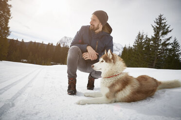 Junger Mann hockt mit Husky in verschneiter Landschaft, Elmau, Bayern, Deutschland - CUF18961