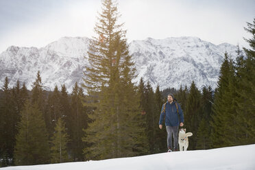 Young man walking uphill with husky in snow covered landscape, Elmau, Bavaria, Germany - CUF18962