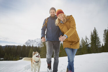 Portrait of couple walking husky in snow covered landscape, Elmau, Bavaria, Germany - CUF18965