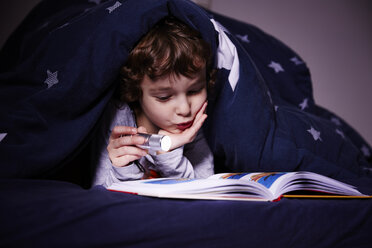 Junge unter der Bettdecke, der bei Fackelschein ein Buch liest - CUF18983