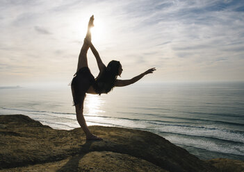 Young female dancer standing on rock, holding leg, stretching in elegant pose, San Diego, California, USA - ISF07259