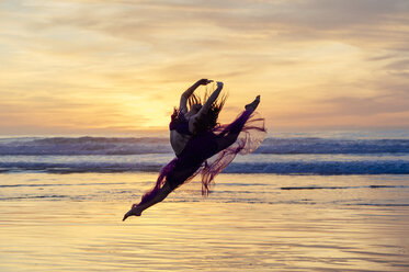 Young female dancer wearing chiffon dress, dancing, in mid air, on beach at sunset, San Diego, California, USA - ISF07261