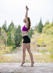 Seitenansicht einer jungen Frau, die am Waldrand eines Sees Yoga übt - ISF07265