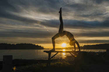 Woman practising yoga by lake at sunset - ISF07269