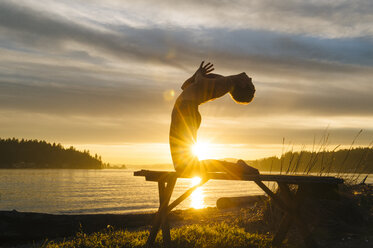 Woman practising yoga by lake at sunset - ISF07270