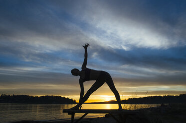 Woman practising yoga by lake at sunset - ISF07273