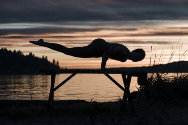 Woman practising yoga by lake at sunset - ISF07274