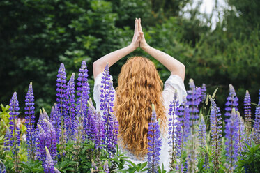 Rear view of young woman meditating with hands together amongst purple wildflowers - ISF07279