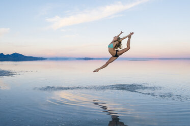 Female ballet dancer leaping mid air over lake, Bonneville Salt Flats, Utah, USA - ISF07282