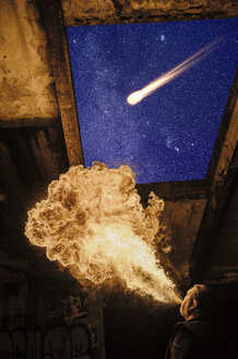 Low angle view of man fire breathing, meteor in starry night sky - ISF07325