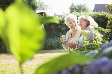 Two women sitting in garden, drinking hot drink, talking - ISF07388