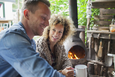 Mid adult couple drinking coffee in open cabin with wood stove - ISF07405