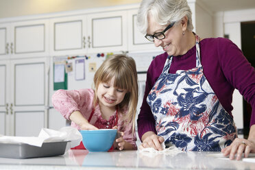 Mädchen und Großmutter mischen Kuchen in einer Schüssel am Küchentisch - ISF07428
