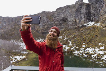 Island, lächelnder bärtiger Mann mit Smartphone, Selfie - AFVF00550