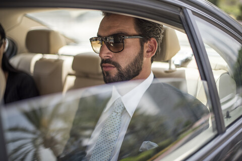 Junger Geschäftsmann mit Sonnenbrille auf dem Rücksitz eines Autos, Dubai, Vereinigte Arabische Emirate, lizenzfreies Stockfoto