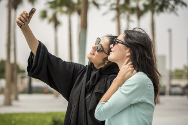 Junge Frau aus dem Nahen Osten in traditioneller Kleidung macht ein Smartphone-Selfie mit einer Freundin, Dubai, Vereinigte Arabische Emirate - CUF19129