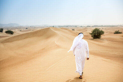 Rückansicht eines Mannes aus dem Nahen Osten in traditioneller Kleidung, der in der Wüste spazieren geht, Dubai, Vereinigte Arabische Emirate - CUF19132