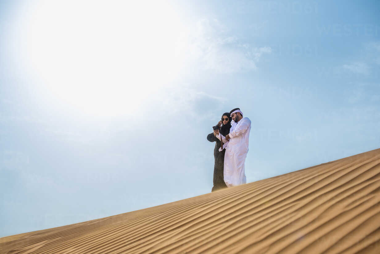 Middle eastern man wearing traditional clothes using smartphone on desert  dune, Dubai, United Arab Emirates stock photo