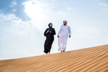 Paar in traditioneller Kleidung aus dem Nahen Osten geht auf einer Wüstendüne spazieren, Dubai, Vereinigte Arabische Emirate - CUF19139