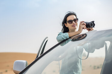Female tourist photographing over off road vehicle in desert, Dubai, United Arab Emirates - CUF19141