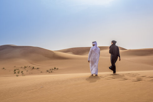 Paar in traditioneller Kleidung aus dem Nahen Osten geht in der Wüste spazieren, Dubai, Vereinigte Arabische Emirate - CUF19144