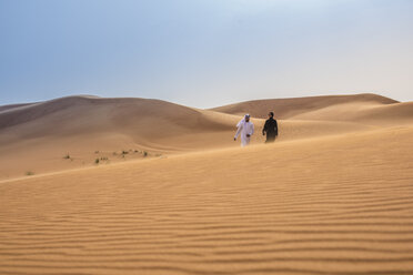 Fernblick auf ein Paar in traditioneller Kleidung aus dem Nahen Osten, das auf einer Wüstendüne spazieren geht, Dubai, Vereinigte Arabische Emirate - CUF19145