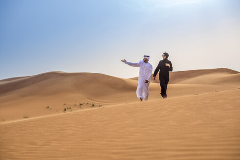 Paar in traditioneller Kleidung aus dem Nahen Osten, das von einer Wüstendüne aus zeigt, Dubai, Vereinigte Arabische Emirate - CUF19146