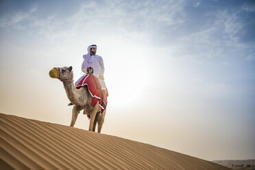 Mann in traditioneller nahöstlicher Kleidung reitet auf einem Kamel in der Wüste, Dubai, Vereinigte Arabische Emirate - CUF19148