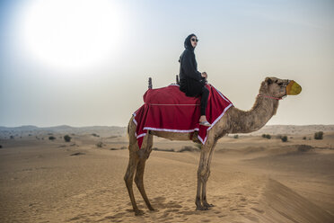 Junge Frau in traditioneller nahöstlicher Kleidung reitet auf einem Kamel in der Wüste, Dubai, Vereinigte Arabische Emirate - CUF19153