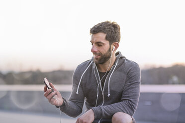 Mid adult man, outdoors, looking at smartphone, wearing earphones - CUF19182