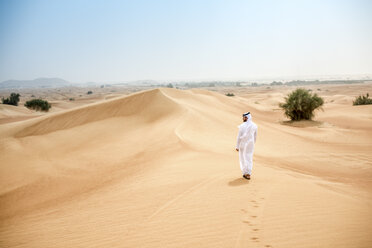 Rückansicht eines jungen Mannes aus dem Nahen Osten in traditioneller Kleidung, der in der Wüste spazieren geht, Dubai, Vereinigte Arabische Emirate - CUF19211