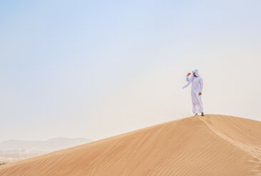 Ein Mann aus dem Nahen Osten in traditioneller Kleidung schaut von einer Wüstendüne aus, Dubai, Vereinigte Arabische Emirate - CUF19213