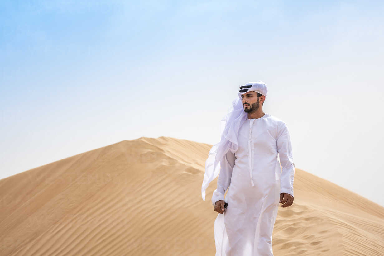 Middle eastern man wearing traditional clothes on desert dune, Dubai,  United Arab Emirates stock photo