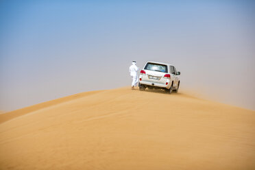 Ein Mann aus dem Nahen Osten in traditioneller Kleidung mit einem Geländewagen, der auf einer Wüstendüne geparkt ist, Dubai, Vereinigte Arabische Emirate - CUF19217