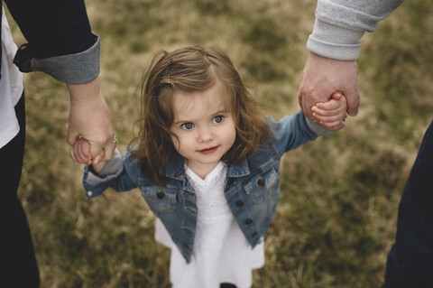 Mutter und Vater halten die Hände ihrer kleinen Tochter, im Freien, Blick von oben, lizenzfreies Stockfoto