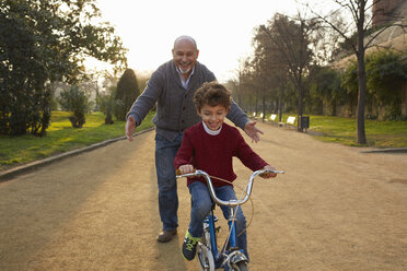 Grandfather teaching grandson to ride bicycle in park - CUF19363