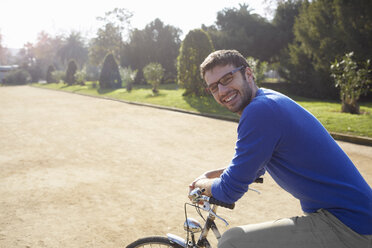 Mittlerer erwachsener Mann sitzt auf einem Fahrrad im Park und schaut lächelnd in die Kamera - CUF19373