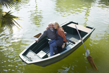 Couple in rowing boat on lake hugging looking at camera smiling - CUF19376