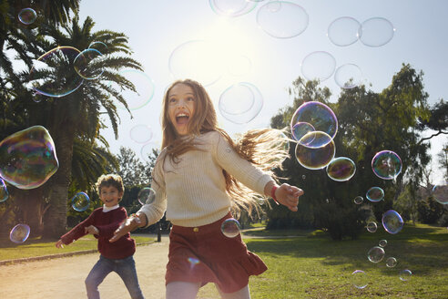 Girl and boy in park running after bubbles - CUF19380