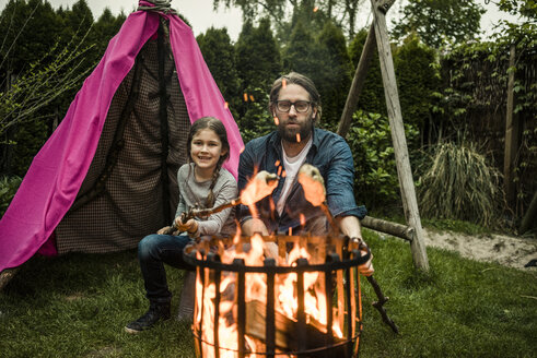 Vater und Tochter grillen Stockbrot über dem Lagerfeuer - MOEF01208