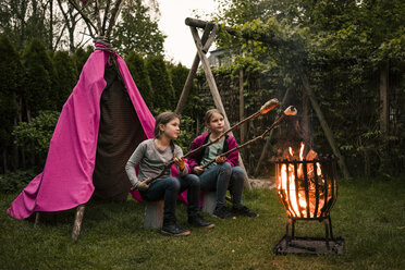 Zwei Mädchen mit Federkopfschmuck, mit Stockbrot am Lagerfeuer - MOEF01211
